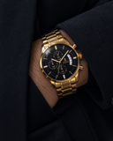 Laguna Drip gold watch with black dial worn with a dark tailored jacket.